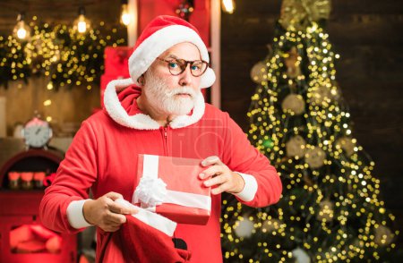 Téléchargez les photos : Funny Santa tenir cadeau de Noël. Le Père Noël souhaite joyeux Noël. Père Noël grand-père avec une barbe blanche posant sur le fond en bois de Noël - en image libre de droit