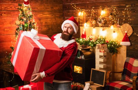 Téléchargez les photos : Hipster en chapeau rouge Santa tenant présent. Cadeaux de livraison. Des émotions cadeaux. Joyeux Noël et Joyeuses Fêtes. Père Noël homme tenant cadeau - en image libre de droit