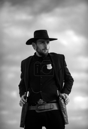 Photo for Sheriff officer in black suit and cowboy hat. Man with wild west guns, vintage pistol revolver and marshal ammunition. US Marshals, American western Sheriff. Wild west with cowboy - Royalty Free Image