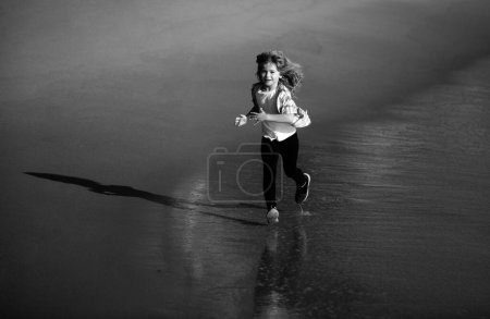 Téléchargez les photos : Un enfant court au bord de la mer. Des enfants qui courent sur la plage. Vacances d'été. Joyeux gamin jouant sur la plage. Bonne enfance. Course et sport sain pour les enfants - en image libre de droit