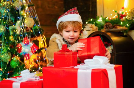 Foto de Lindo niño pequeño está decorando el árbol de Navidad en el interior. Lindos niños celebrando la Navidad. Lindo niño pequeño cerca del árbol de Navidad - Imagen libre de derechos