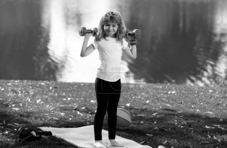 Photo for Sport child with strong biceps muscles. Kids exercising fitness dumbbells. Strong little boy exercising with dumbbell in park outdoor. Sport strong boy, little bodybuilder - Royalty Free Image