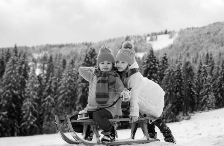 Téléchargez les photos : Luge garçon et fille dans une forêt enneigée. Hiver plein air enfants amusant pour Noël et le Nouvel An. Les enfants profitent d'une promenade en traîneau. Paysage de Noël - en image libre de droit