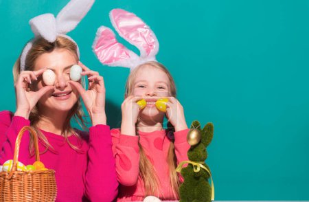 Téléchargez les photos : Portrait de mère avec fille portant des oreilles de lapin avec décoration des œufs de Pâques isolés sur bleu - en image libre de droit