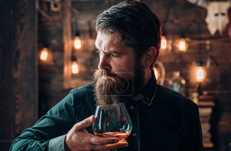 Photo for Man with alcohol drink at home. Bearded man sitting at bar. Alcoholic with bottle and glass drinking cognac at night - Royalty Free Image