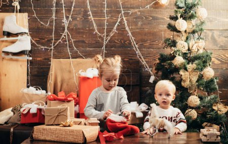 Téléchargez les photos : Les enfants d'hiver. Carte de Noël. Des petits enfants mignons qui fêtent Noël. Joyeux bébé regardant la caméra à Noël à la maison. Cadeaux d'ouverture à Noël et Nouvel An - en image libre de droit