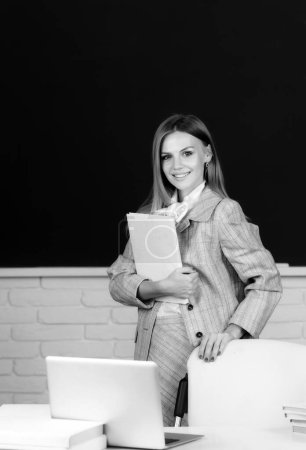 Foto de Hermosa estudiante sosteniendo libro en el fondo de pizarra, linda mujer joven rubia en clase en la escuela - Imagen libre de derechos