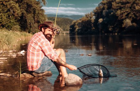 Photo for Young bearded man fishing at a lake or river. Flyfishing - Royalty Free Image