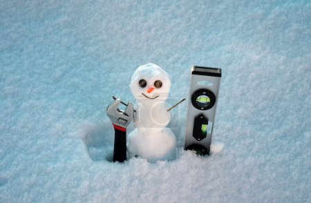 Foto de Snow man. Repairman with repair tools. Support repair and recover service. Snowman isolated on snow background - Imagen libre de derechos