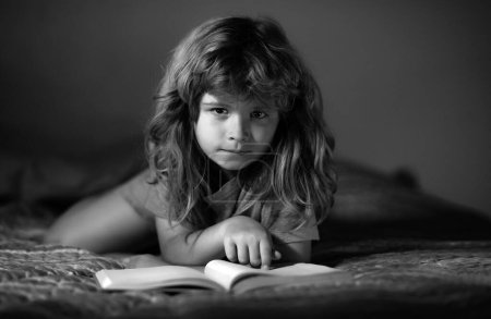 Téléchargez les photos : Des enfants lisant un livre dans le noir. Visage d'enfant avec veilleuse. Concept d'éducation et de lecture. Les enfants le développement de l'imagination. Enfant garçon lisant un livre allongé sur le lit - en image libre de droit