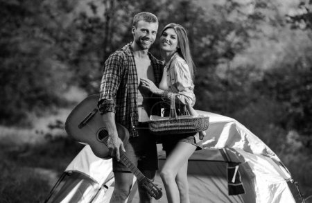 Foto de Pareja acampando. Coupl joven en campamento campestre, hombre con guitarra. Pareja enamorada. Novia y novio en fin de semana romántico en la naturaleza. Picnic para amigos turistas - Imagen libre de derechos