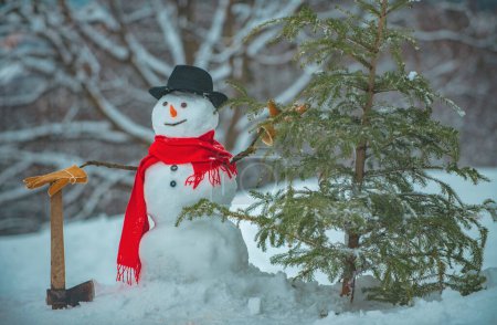 Photo for Snowman with freshly cut down christmas tree in forest. Young snowman lumberjack bears fir tree in the white snow background - Royalty Free Image
