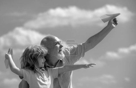 Téléchargez les photos : Vieux grand-père et jeune petit-fils avec avion en papier sur ciel bleu et nuages. Hommes génération grand-père et petit-enfant - en image libre de droit