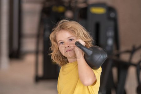 Photo for Kid workout kid in gym. Cute child boy pumping up arm muscles with kettlebell dumbbell. Fitness kids with dumbbells - Royalty Free Image