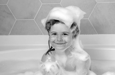 Foto de Niños bañándose. Niño con espuma de champú y burbujas en el baño de pelo. Cara divertida de niño en espuma, cuidado del cabello y concepto de higiene. Champú para cabellos largos. Lavado del cabello en el baño - Imagen libre de derechos