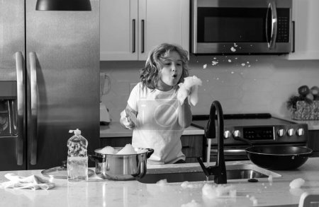 Foto de Niños lavando platos cerca del fregadero en la cocina. Niño con esponja con líquido de lavado de platos está lavando los platos en la cocina del hogar mediante el uso de esponja de lavado y lavado de platos - Imagen libre de derechos