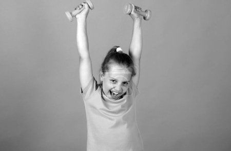 Photo for Excited sport and fitness girl, kids health and energy. Healthy children lifestyle. Cheerful boy do exercises with dumbbells. Girl exercising with dumbbells in studio, isolated. Sport portrait kids - Royalty Free Image