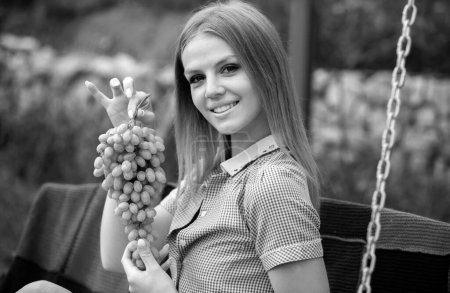 Foto de Hermosa joven muerde de racimos de uva, contra el parque verde de verano. Vino hecho a mano de uva blanca. Una joven muy sexy sosteniendo un ramo de uva en su cara - Imagen libre de derechos