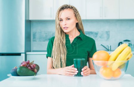 Photo for Blended green and orange smoothie with healthy fruits ingredients. Woman with glass of natural detox smoothie in kitchen. Weight loss. Vegan vegetarian vegetable concept. Spirulina for weight loss - Royalty Free Image