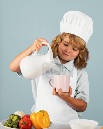 Photo for Milk for children. Kid boy in chef hat and apron cooking preparing meal. Little cook with vegetables at kitchen. Natural kids food - Royalty Free Image