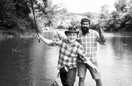 Téléchargez les photos : Deux hommes amis pêcheur pêche sur la rivière. Vieux père et fils avec canne à pêche au bord de la rivière. Activités récréatives - en image libre de droit