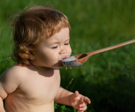 Photo for Feeding baby with big spoon outdoor on green grass - Royalty Free Image