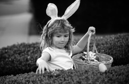 Foto de Niños en orejas de conejo en la búsqueda de huevos de Pascua en el jardín. Niño recogiendo huevos, concepto de caza de huevos de Pascua. Feliz cara de niños de Pascua - Imagen libre de derechos