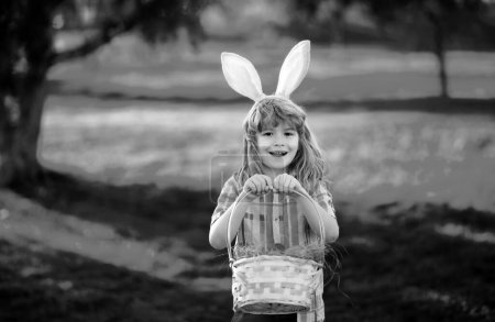Téléchargez les photos : Joyeuses Pâques pour les enfants. Enfant garçon en costume de lapin avec des oreilles de lapin chasse oeufs de Pâques dans le parc - en image libre de droit