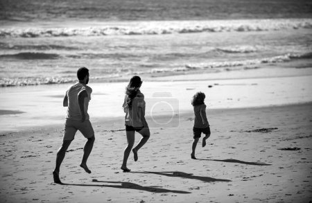 Téléchargez les photos : Joyeux jeune famille courir et sauter sur la plage d'été. Enfant dont les parents courent et sautent. Voyage en famille, concept de vacances - en image libre de droit