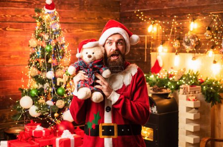 Photo for Hipster Santa at home. Bearded man having fun near Christmas tree indoors. Home Christmas atmosphere. Men in winter clothes. Santa winter portrait - Royalty Free Image