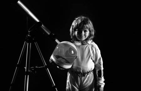 Téléchargez les photos : Petit garçon portant un costume d'astronaute et un télescope. Joli gamin astronaute jouant et rêvant de devenir astronaute. Concept d'astronomie et d'astrologie - en image libre de droit