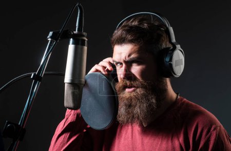 Photo for Portrait of singer wearing headphones is performing a song with a microphone while recording in a music studio - Royalty Free Image