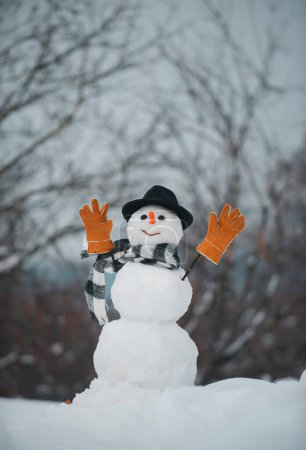 Foto de Descuentos de venta de Navidad. Hombre de nieve. Muñeco de nieve con estrella de la luz en Navidad. Muñeco de nieve divertido en sombrero elegante y bufanda en el campo cubierto de nieve - Imagen libre de derechos