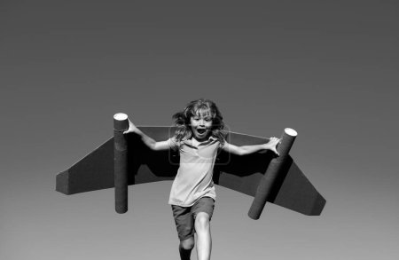 Photo for Kid with jet pack superhero. Child pilot against summer sky background. Boy with paper plane flight, toy airplane with cardboard wings, Imagination, kids freedom - Royalty Free Image