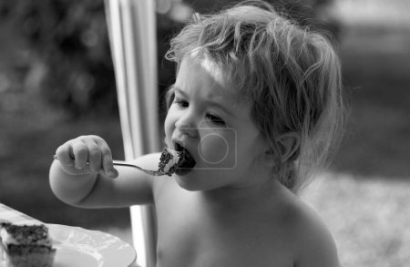 Téléchargez les photos : Un bébé qui mange du gâteau. Mignon enfant mange délicieux à l'extérieur - en image libre de droit