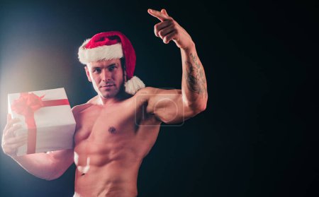 Photo for Sexy shirtless Santa with gift on black background, space for text - Royalty Free Image