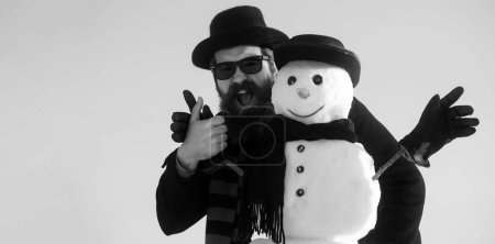 Téléchargez les photos : Portrait d'un homme joyeux profitant d'une journée enneigée froide. Humour hiver bonhomme de neige en chapeau jouer avec bonhomme de neige en plein air. Homme avec bonhomme de neige sur fond d'hiver extérieur. Bonhomme de neige pour bannière d'hiver - en image libre de droit