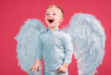 Téléchargez les photos : Portrait de petit garçon ange blond bouclé et souriant heureux. Enfant angélique. Bébé portant ange robe blanche costume et ailes de plumes. Consept d'enfant innocent - en image libre de droit