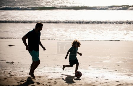 Foto de Padre e hijo juegan fútbol o fútbol en la playa. Papá y el niño jugando al aire libre. Concepto de infancia y crianza - Imagen libre de derechos