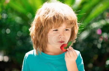 Téléchargez les photos : Happy child mange des fraises en été en plein air - en image libre de droit