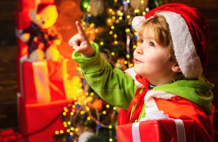 Photo for Boy cute child cheerful mood play near christmas tree. Gifts for winter holidays near fire place. Christmas eve. Kid at Christmas tree and fireplace on Xmas eve - Royalty Free Image