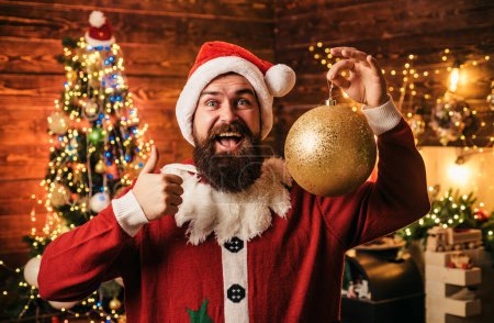Foto de Loco, divertido Hipster Santa. Retrato de Papá Noel feliz con pelotas de juguete decorativas cerca del árbol de Navidad. Feliz Papá Noel vestido con ropa de invierno pensar en la Navidad o Año Nuevo - Imagen libre de derechos