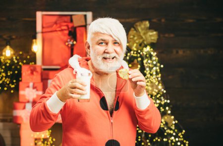 Foto de Papá Noel en casa. Santa recogiendo galletas y un vaso de leche en casa. Estilo barba de Navidad. Retrato de Santa Claus Beber leche de vidrio y sostener galletas - Imagen libre de derechos