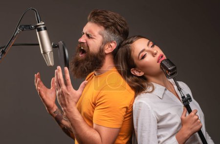 Téléchargez les photos : Couple chanteur chantant rock. Producteur sonore enregistrant une chanson dans un studio de musique. Duo excité Karaoké - en image libre de droit