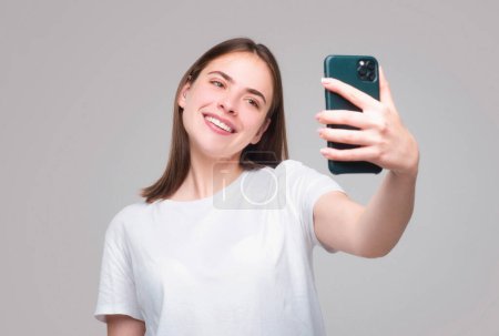Photo for Happy young african woman casually dressed standing isolated over gray background, holding mobile phone. Girl making taking selfie - Royalty Free Image