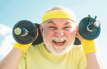Foto de Hombre mayor de setenta años entrenando y levantando pesas. Club de salud o centro de rehabilitación para jubilados de edad avanzada. Hombre de deporte senior levantando pesas en el centro deportivo - Imagen libre de derechos