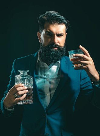 Foto de Atractivo camarero en el bar de whiskey. Elegante hombre rico sosteniendo un vaso de whisky viejo. Hombre con barba sostiene brandy de vidrio - Imagen libre de derechos