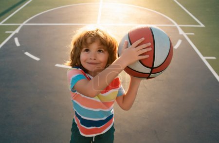 Foto de Lindo chico sonriente juega baloncesto. Niños activos disfrutando de juego al aire libre con pelota de cesta. Vista superior - Imagen libre de derechos