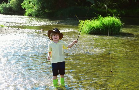 Téléchargez les photos : Petit enfant pêchant sur la rivière. Garçon en chemise jaune avec une canne à pêche près de la rivière. Pêcheur enfant en utilisant la canne à pêche dans la belle rivière - en image libre de droit