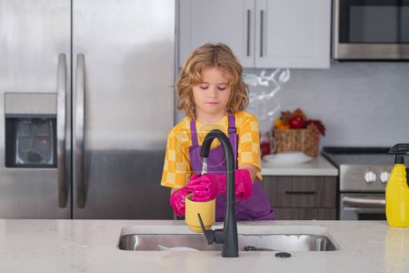 Photo for Portrait of child cleaning in the kithen. Child housekeeper washing the dishes on soapy water. Cute Funny boy washing dishes in kitchen - Royalty Free Image
